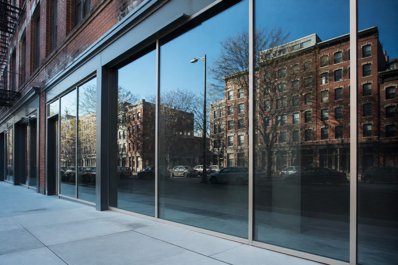 Glazed facade reflecting a clear sky above a Brooklyn sidewalk